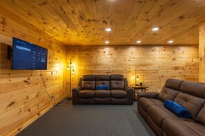 A wooden-paneled room with a leather sofa, a television mounted on the wall, and a small table with a lamp. - Moonlight Ridge Lodge - Hocking Hills (Logan)