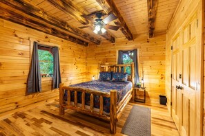 A wooden cabin bedroom with a bed, a ceiling fan, and a window with curtains. - Moonlight Ridge Lodge - Hocking Hills (Logan)