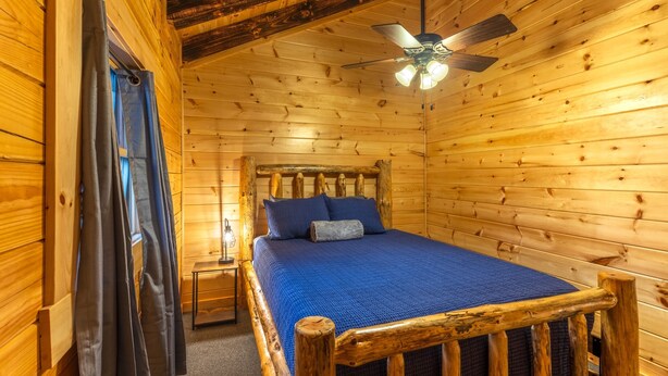 A wooden cabin bedroom with a bed, a ceiling fan, and a nightstand. - Moonlight Ridge Lodge - Hocking Hills (Logan)
