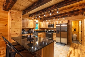 A modern log cabin kitchen with wooden walls, a central island, stainless steel appliances, and a hanging light fixture. - Moonlight Ridge Lodge - Hocking Hills (Logan)