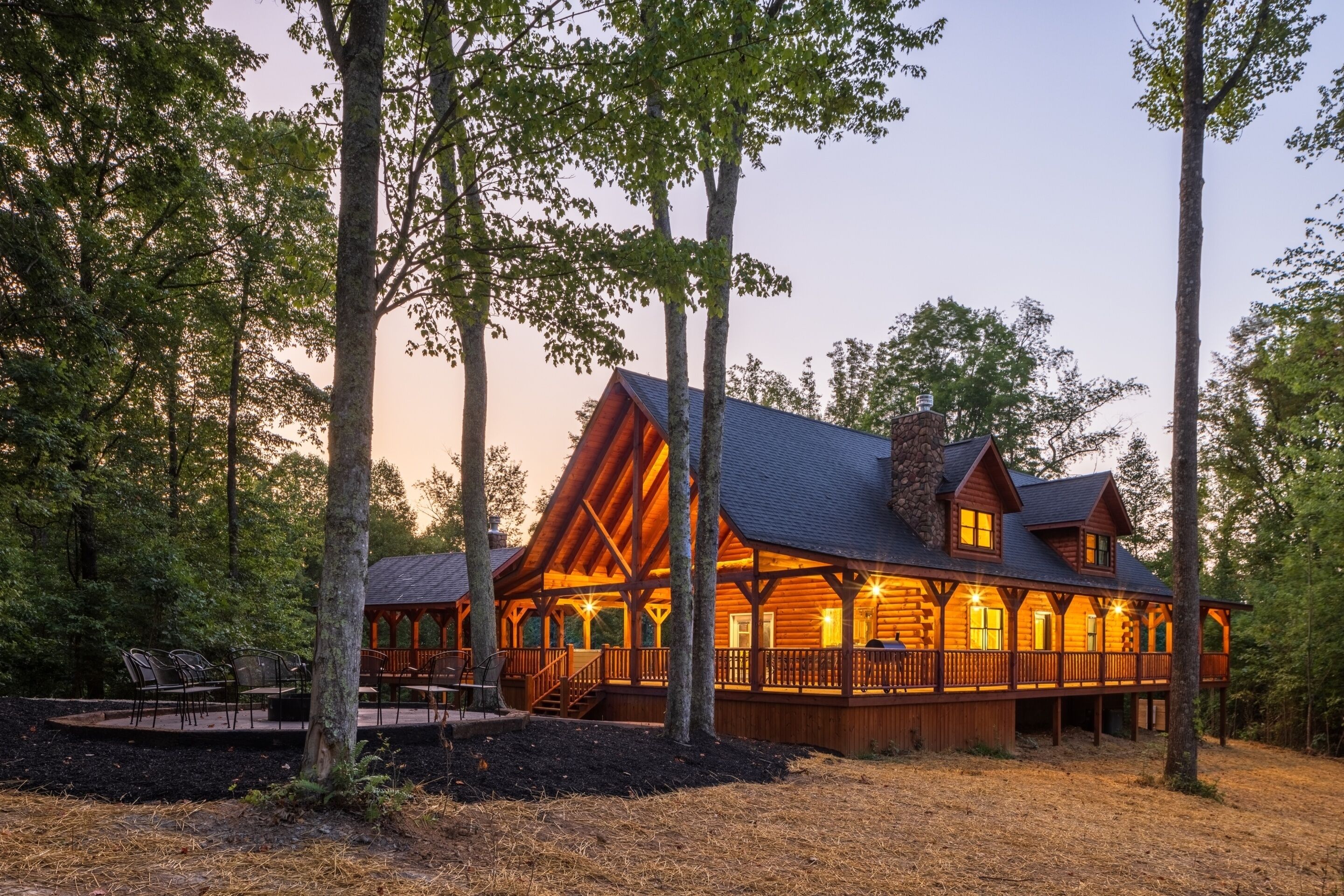 A log cabin with a covered porch and multiple windows, surrounded by trees.