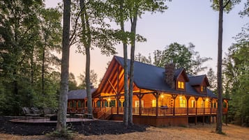 A log cabin with a covered porch and multiple windows, surrounded by trees.