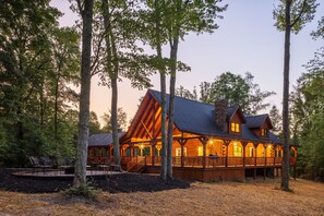 A log cabin with a covered porch and multiple windows, surrounded by trees.