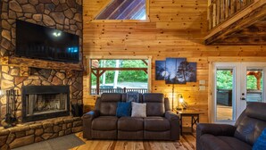 L’intérieur chaleureux d’un chalet avec une cheminée en pierre, un canapé en cuir et un téléviseur fixé au mur.