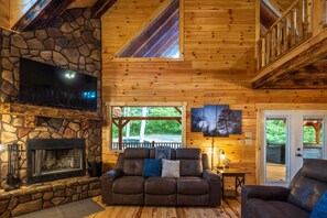 A cozy cabin interior with a stone fireplace, a leather sofa, and a television mounted on the wall. - Moonlight Ridge Lodge - Hocking Hills (Logan)