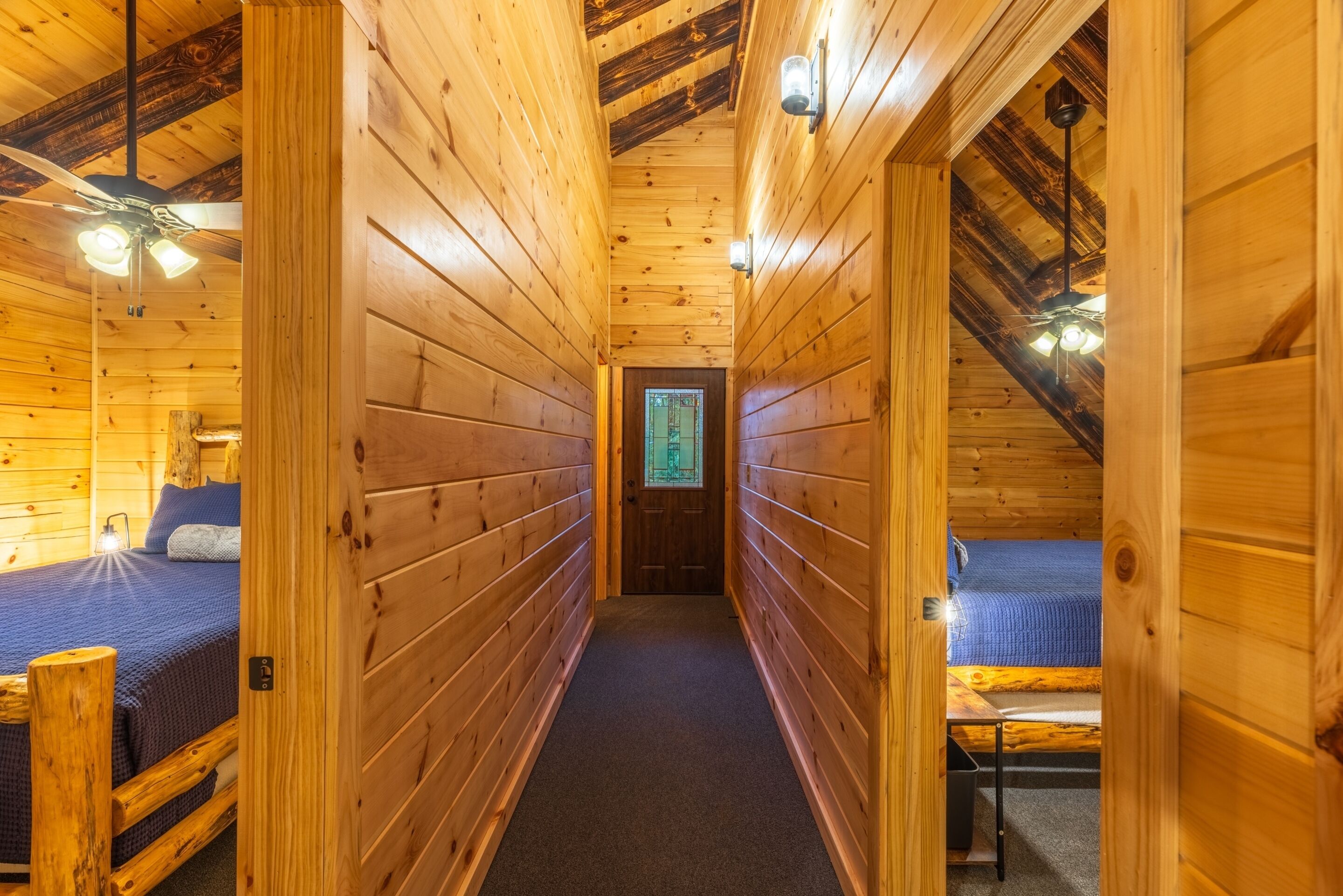 A narrow wooden hallway with two beds on either side, a ceiling fan, and a door at the end.