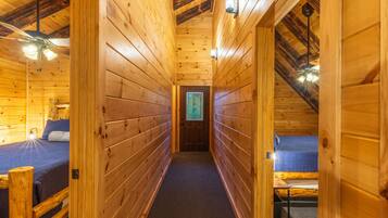 A narrow wooden hallway with two beds on either side, a ceiling fan, and a door at the end.