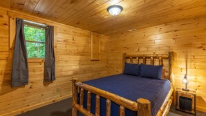 Une chambre rustique en bois, avec un lit, une fenêtre avec des rideaux et une table de chevet avec une lampe.