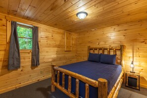 A wooden cabin room with a bed, a window with curtains, and a nightstand with a lamp. - Moonlight Ridge Lodge - Hocking Hills (Logan)