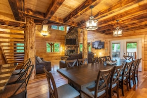 A rustic cabin interior with a large dining table, wooden walls, and a stone fireplace. - Moonlight Ridge Lodge - Hocking Hills (Logan)