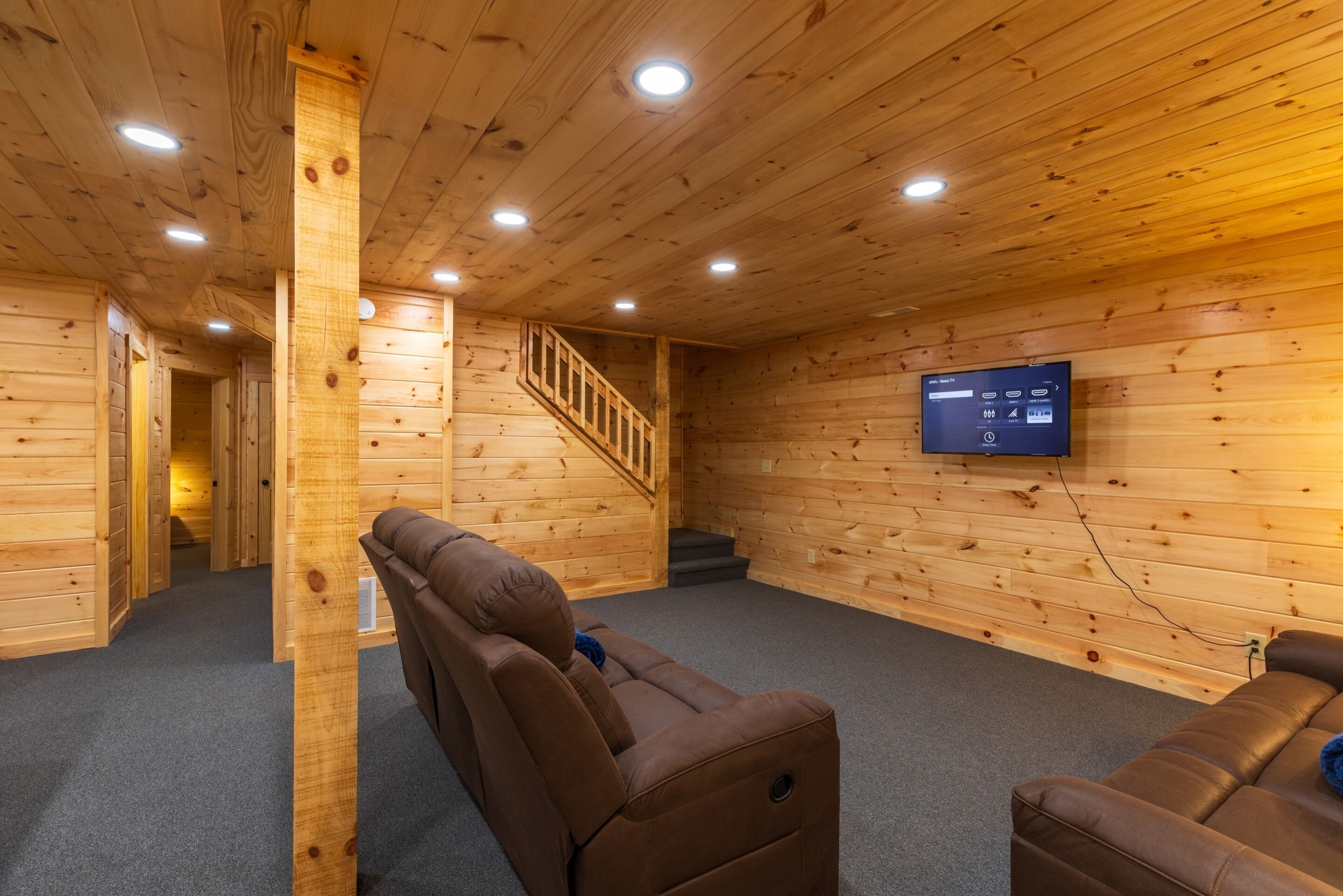 A wooden interior with a sofa, a TV mounted on the wall, and a staircase.