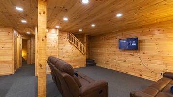 A wooden interior with a sofa, a TV mounted on the wall, and a staircase.
