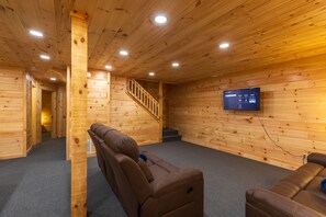 A wooden interior with a sofa, a TV mounted on the wall, and a staircase.