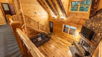 A wooden cabin interior with a stone fireplace, a wooden staircase, and a cozy seating area.