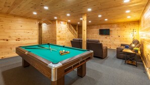 Une pièce aux murs lambrés, avec une table de billard, un canapé et une petite table sur laquelle se trouve une lampe.