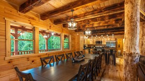 A wooden cabin interior with a dining area, kitchen, and large windows offering a view of the forest. - Moonlight Ridge Lodge - Hocking Hills (Logan)