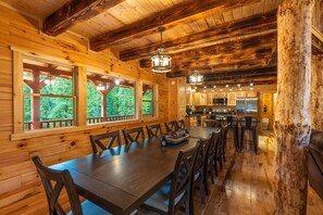 A wooden cabin interior with a dining area, kitchen, and large windows offering a view of the forest. - Moonlight Ridge Lodge - Hocking Hills (Logan)