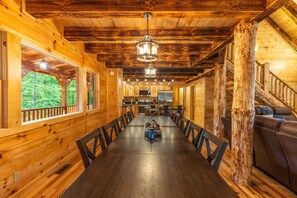 A wooden cabin interior with a long dining table, chairs, a kitchen area, and a staircase. - Moonlight Ridge Lodge - Hocking Hills (Logan)