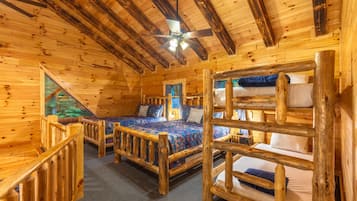 A cabin with a wooden interior, two bunk beds, a ceiling fan, and a window with a view of trees.