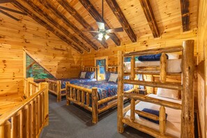 A cabin with a wooden interior, two bunk beds, a ceiling fan, and a window with a view of trees.