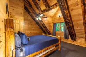 A wooden cabin bedroom with a bed, a ceiling fan, and a window. - Moonlight Ridge Lodge - Hocking Hills (Logan)