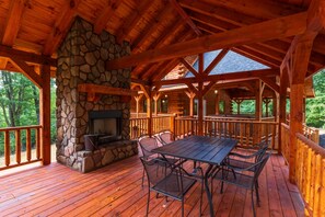 A wooden deck with a stone fireplace, metal chairs, and a table. - Moonlight Ridge Lodge - Hocking Hills (Logan)