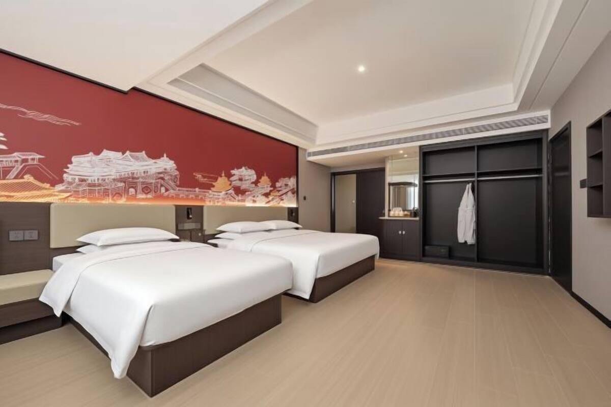 A modern hotel room with two beds, a large mural, a wardrobe, and a mirror.