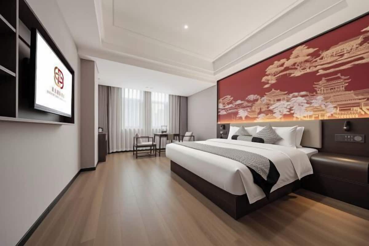 A hotel room with a large bed, a desk, and a TV mounted on the wall.