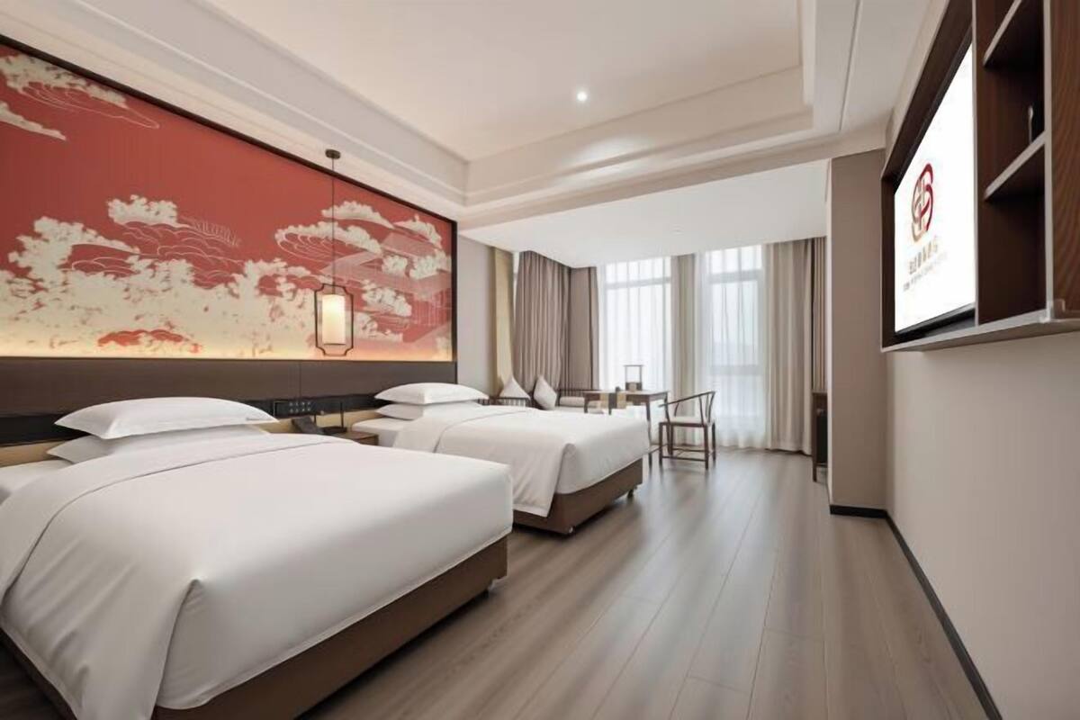 A hotel room with three beds, a large wall mural, a desk, and a TV.