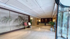 Un hall d’hôtel moderne avec un comptoir d’accueil en bois, une cloison en verre et des plantes en pot.