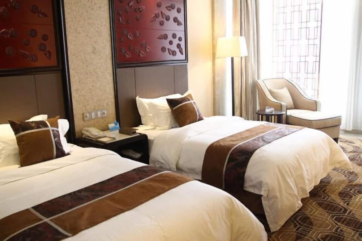 A hotel room with two beds, a desk, a chair, and a patterned carpet.