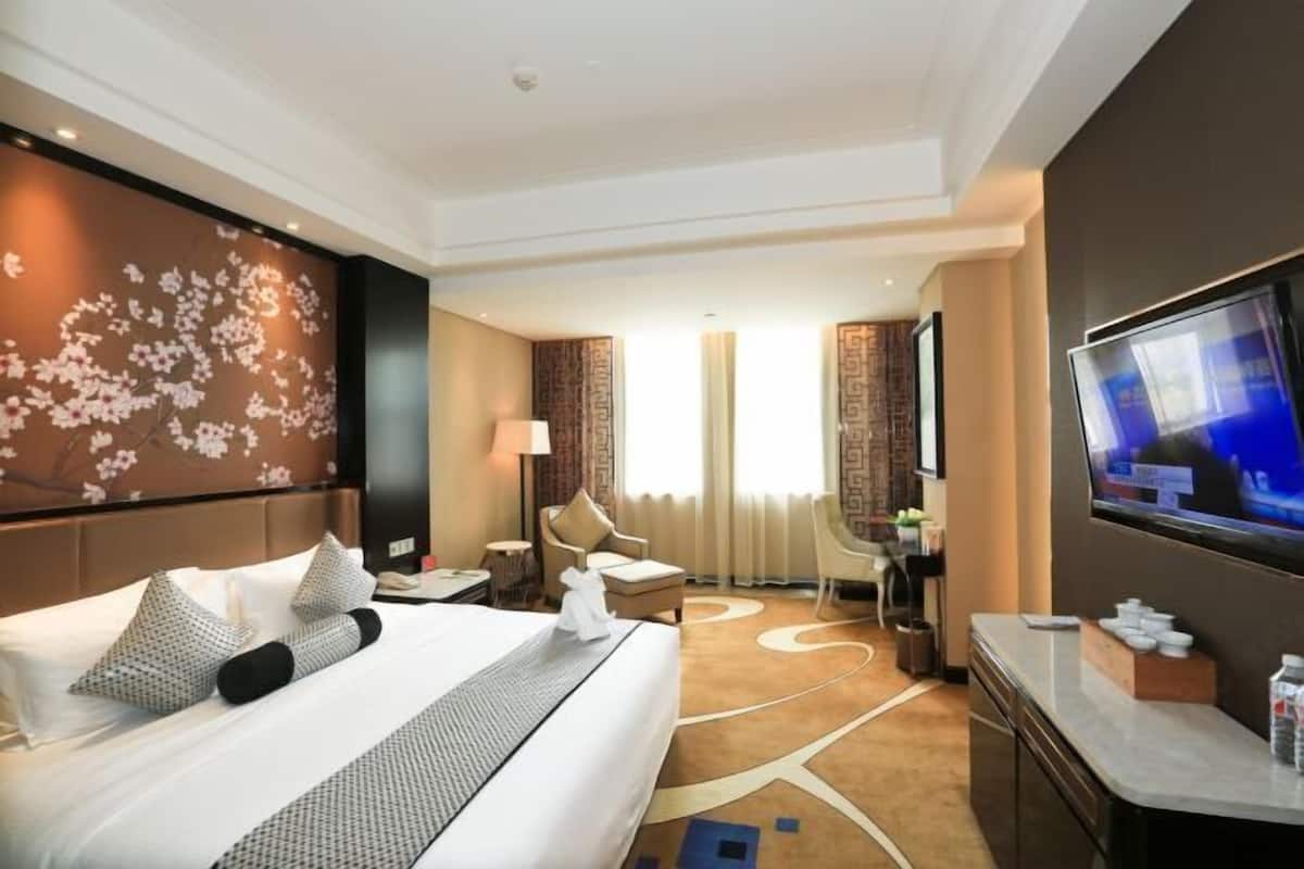 A hotel room with a bed, a desk, a chair, a TV, and a wall with a floral design.