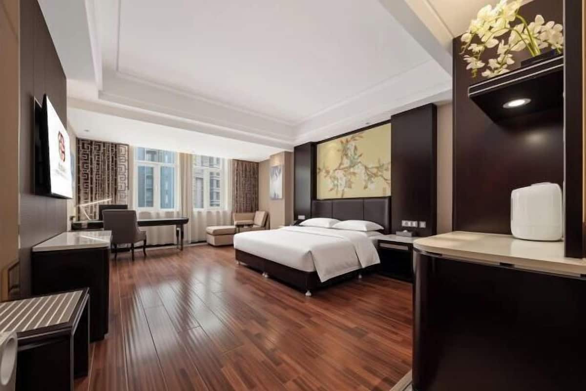 A hotel room with a bed, desk, chair, and a large window.