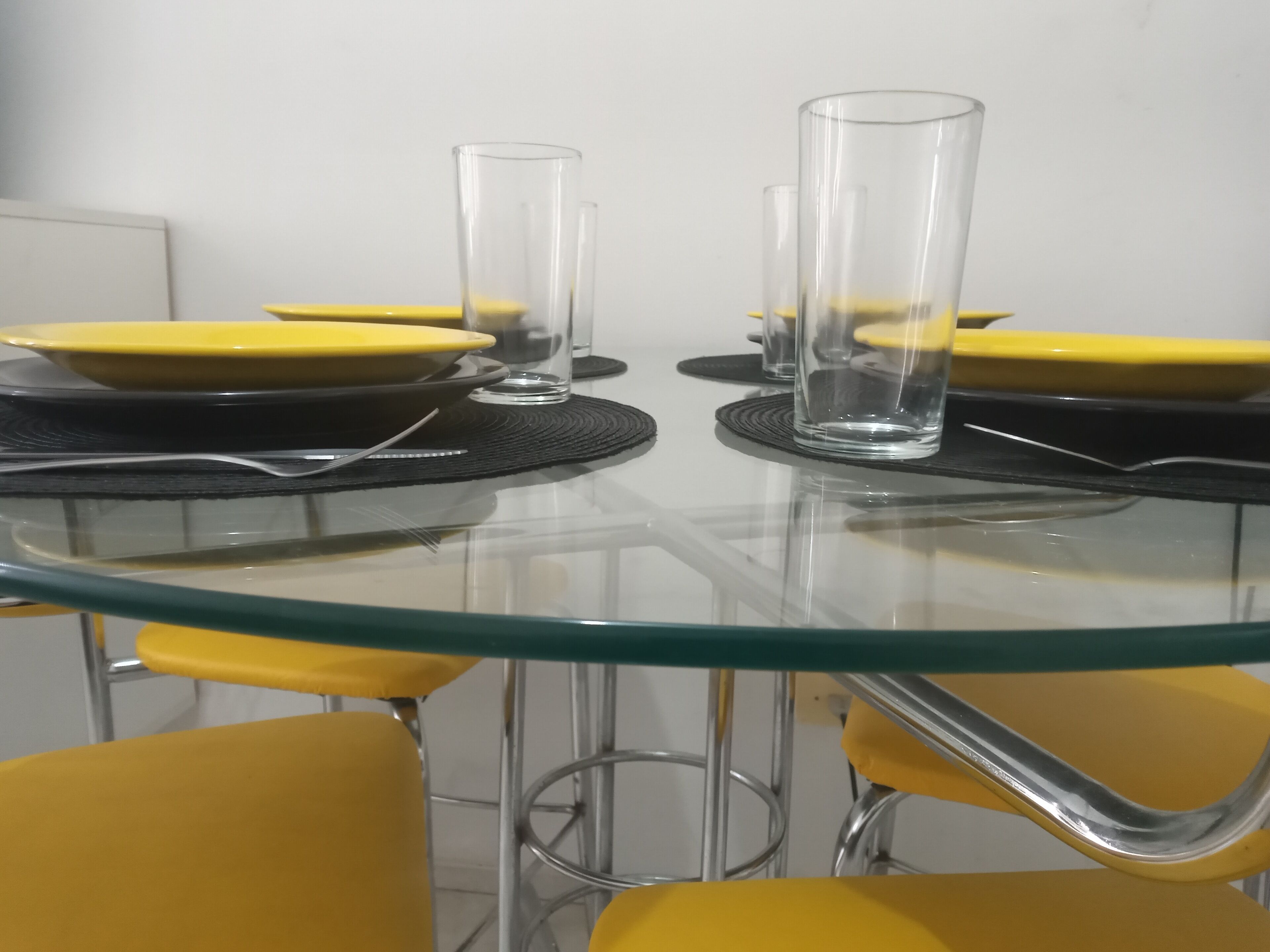 Una mesa redonda de cristal con sillas amarillas, cubiertos de vidrio transparente y caminos de mesa negros.