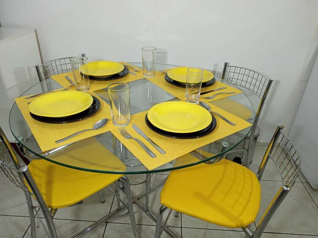 Una mesa redonda de vidrio con individuales amarillos y sillas a juego en color amarillo.