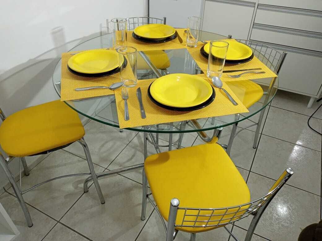 Una mesa de vidrio redonda con manteles individuales amarillos, sillas amarillas a juego y cuatro platos preparados.