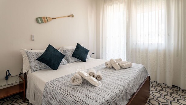 Ein ordentlich bezogenes Bett mit aufgerollten Handtüchern, einer Holzofen-Wanddekoration und einem Fenster mit transparenten Vorhängen.