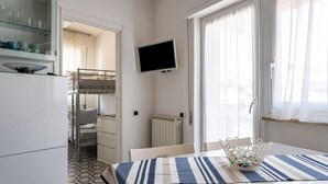 Ein Zimmer mit einem Etagenbett, einem an der Wand montierten Fernseher, einem Tisch mit gestreifter Tischdecke und einem Fenster mit Vorhängen.