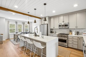 A modern kitchen with a central island, stainless steel appliances, and a large window providing a view of the outdoors.
