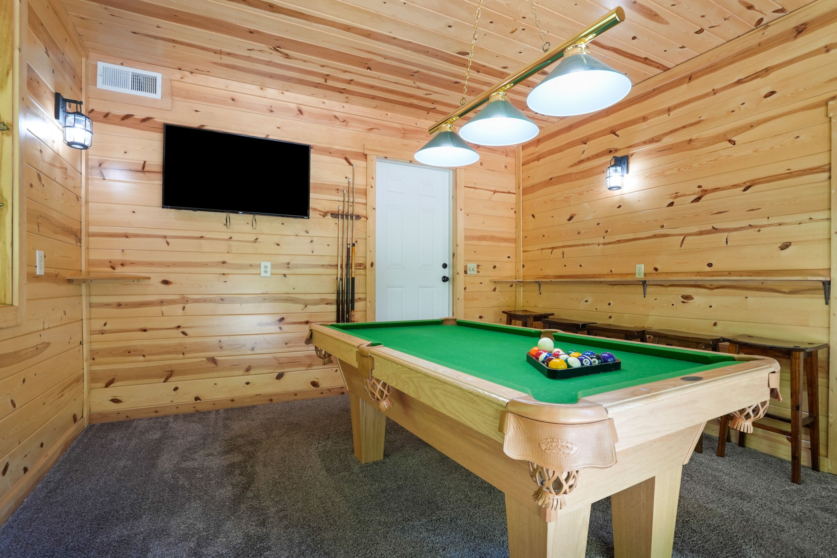 Een pooltafel met een groene viltkleed, omringd door houten wanden en een plafond met houten balken.