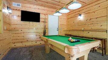 Een pooltafel met een groene viltkleed, omringd door houten wanden en een plafond met houten balken.