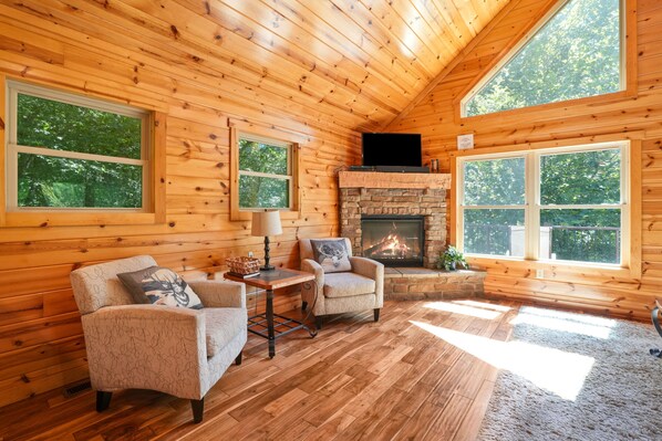 A cozy cabin with wooden walls, a stone fireplace, and two armchairs.