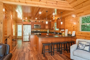 Interior de una cabaña de madera con cocina, barra y zona de estar.