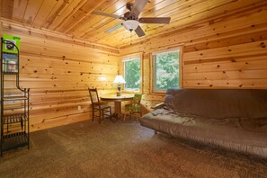 Un acogedor interior de cabaña con paredes de madera, un ventilador de techo, una mesa redonda con sillas y un sofá.
