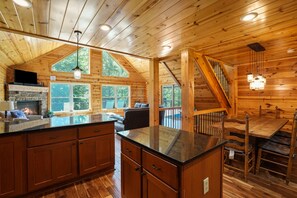 A log cabin interior with a kitchen, dining area, and a fireplace.