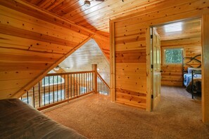 A cabin with a loft bedroom, a wooden staircase, and a view of the outdoors.