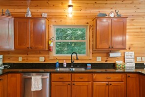 A wooden cabin kitchen with a large window, wooden cabinets, a stainless steel sink, and a dish drying rack.