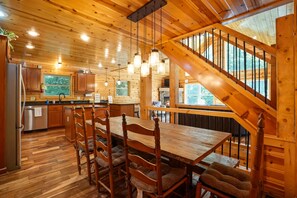 A wooden cabin interior with a dining area, kitchen, and a staircase. - Scenic Solitude | Private Pond, Hot Tub, Game Room (Laurelville)