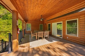 A wooden deck with a table and chairs, large windows, and a ceiling fan. - Scenic Solitude | Private Pond, Hot Tub, Game Room (Laurelville)