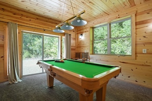 Eine Holzhütte mit Pooltisch, großen Fenstern und einer Deckenleuchte.